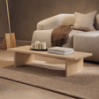 Mesa de centro baja de madera clara con patas tipo panel, en un living con sofá beige
