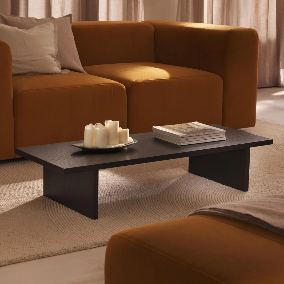 Mesa de centro de madera teñida negra, en un living con sofá naranjo