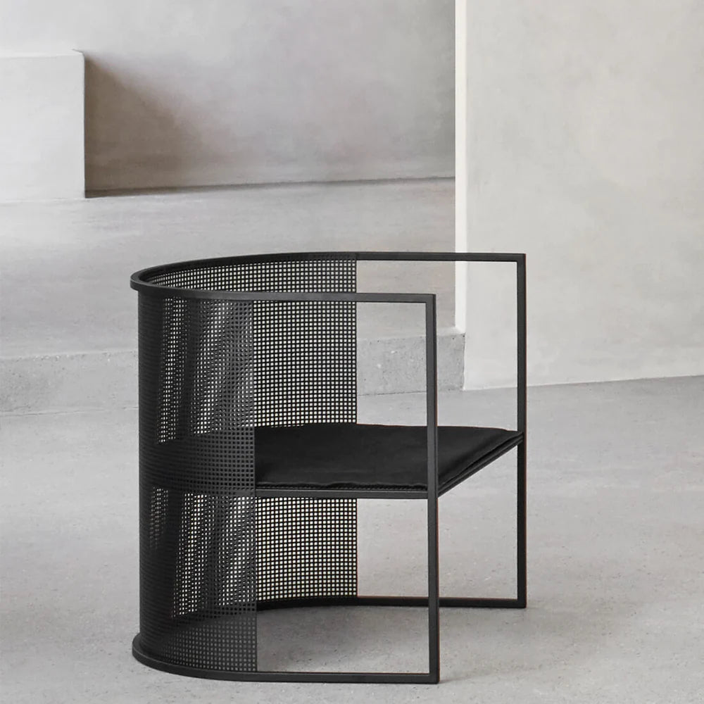 Silla individual de acero perforado negro con asiento acolchado, en una sala de muros de hormigón