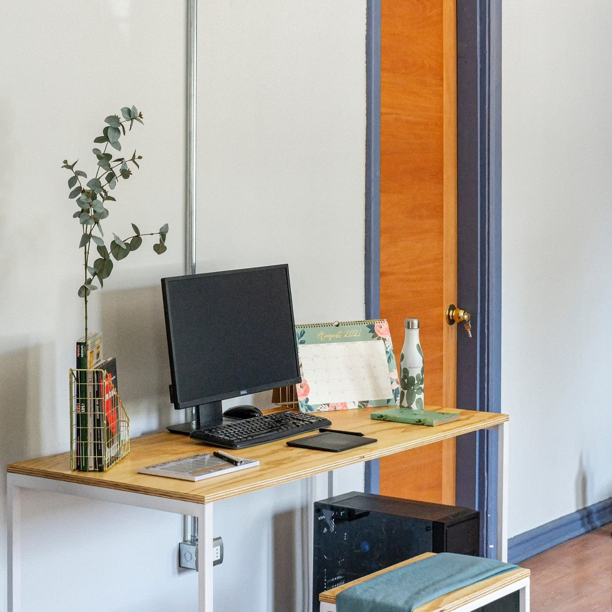 Escritorio de estructura blanca y cubierta de abedul con monitor, teclado y un florero, en una oficina en casa