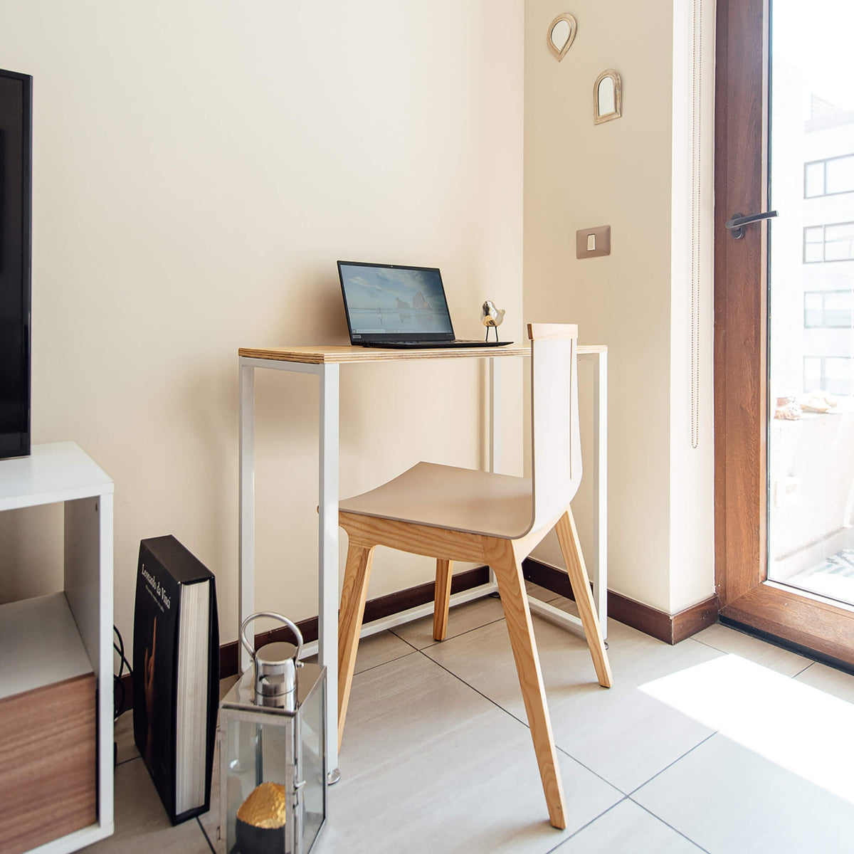 Escritorio de estructura blanca y cubierta de abedul junto a una ventana, con notebook y silla de madera