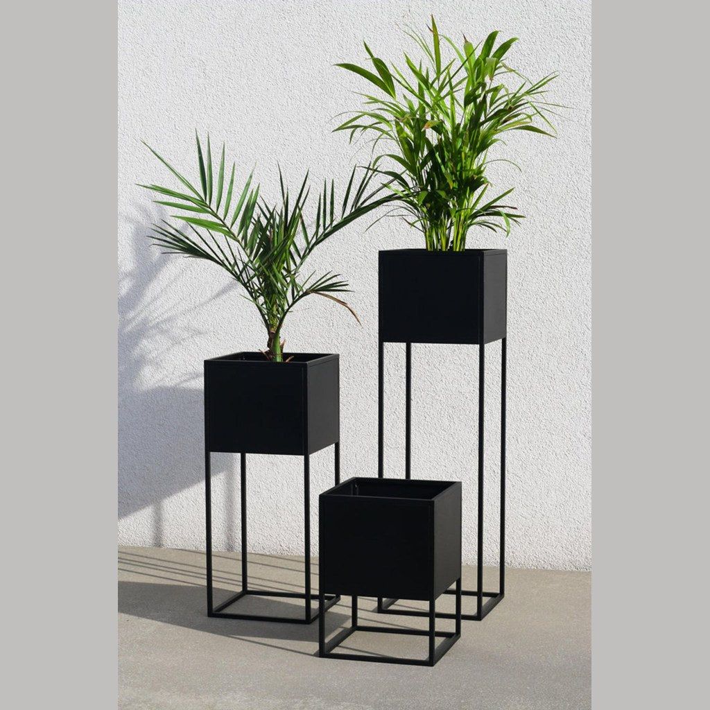 Tres maceteros Bailey Kallfü negros de distintas alturas, ambientados con plantas