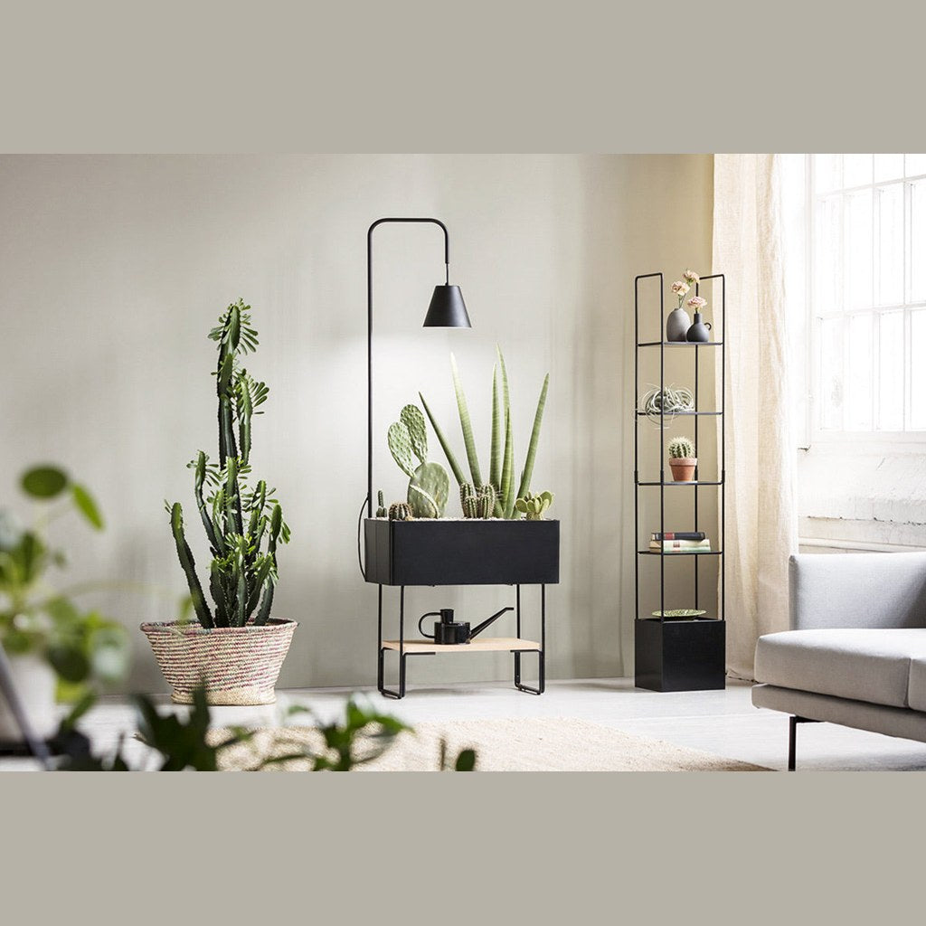 Macetero torre Pentagon Kallfü negro en un living con plantas y lámpara