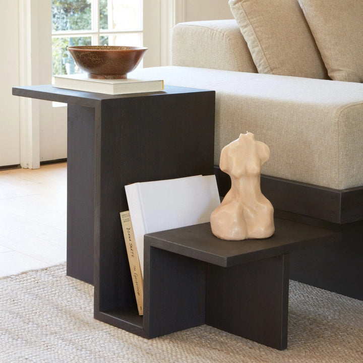 Mesa lateral Skyline en madera teñida negra junto a un sofá, con un bol y un libro arriba y una revista en la ranura